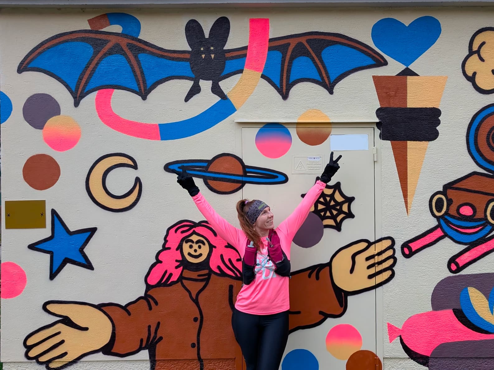 Marion steht vor einer Wand mit buntem Graffiti und streckt fröhlich die Arme in die Höhe.