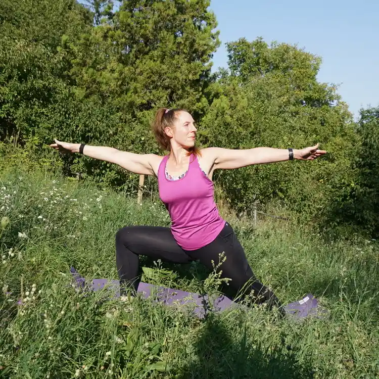 Marion macht auf einer Blumenwiese die Yogapose Krieger 2.